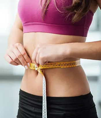 A woman holds tape measure around her midsection.